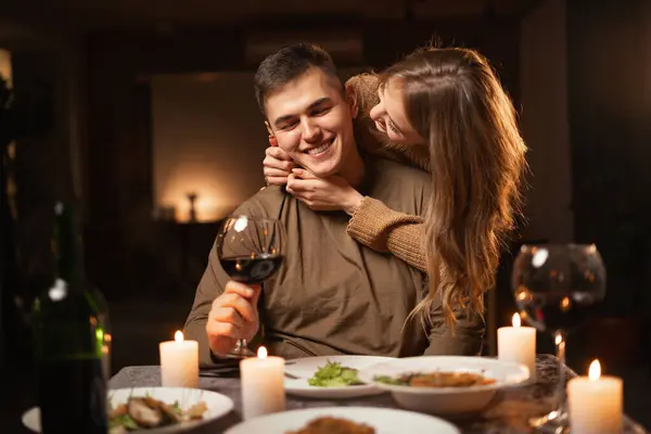 Happy couple kissing during dinner date, relationship affection at night at home. Girl kissing man cheers in romance on dining, celebration anniversary or valentines day. Copy space