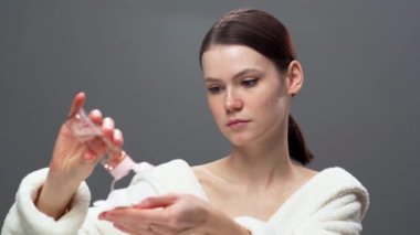 Pamuklu ped ve mikiler suyuyla makyaj yapan hoş bir kadın. Gri arka planda mükemmel bir cildi olan kız. Güzellik ve cilt bakımı. Boşluğu kopyala