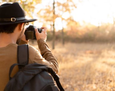 Erkek turist doğayı fotoğraflıyor. Şapkalı, kameralı ve sonbahar ormanında yürüyüş yapan bir adam. Boşluğu kopyala