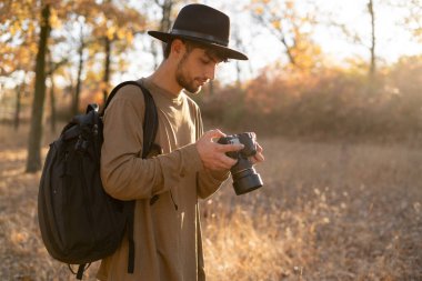 Sonbahar ormanı, fotoğraf ve macera konseptinde gülümseyen ve elinde dijital kamerayla gezen Arap genç fotoğrafçı. Boşluğu kopyala