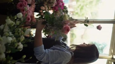 Çiçekçi dükkanında çiçek buketi yapan ve tasarlayan bir kadın. Dikey video