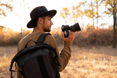 Doğa fotoğrafçılığı konsepti. Dijital kamerası ve arka planında sonbahar ormanı olan profesyonel doğa fotoğrafçısı. Boşluğu kopyala