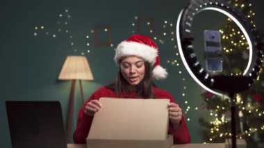 Noel Baba şapkası takan çekici bir kadın blogcu kameraya dijital tabletle kutusunu açıyor ve Noel 'de evdeki teknoloji blogu için video içeriği kaydediyor. Boşluğu kopyala