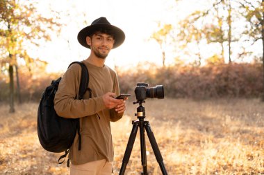 Cep telefonlu seyahat fotoğrafçısı sonbaharda günbatımında doğayla fotoğraf çekiyor. Doğal fotoğrafçılık rahatlatıcı bir kavram.