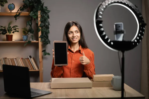 Blogger recording a video review of a modern tablet on a smartphone camera in a home studio, social media influencer advertising a technology product. Copy space