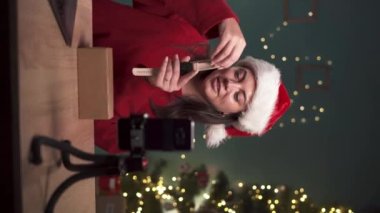 Kadın blogcu, teknoloji video blogunu kaydediyor, yeni ukala kasetçaları açıyor, akıllı telefondan evde tripodla konuşuyor. Sosyal medya yayını, yeni yıl, Noel konsepti. dikey video