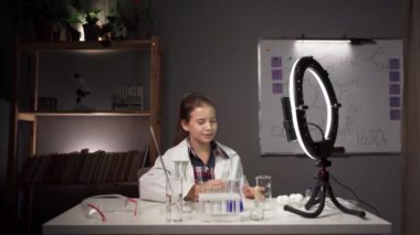 Kimya okuyorum. Beyaz laboratuvar önlüğü giymiş, kimya okuyan çocuk blogcu deney videosu çekiyor. Boşluğu kopyala