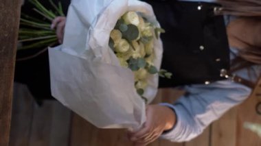 Çiçekçi beyaz güllerde güzel bir buket yapıyor ve el işi kağıdına sarılıyor. Uzayı kopyala Dikey video