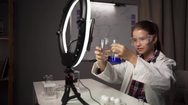 かわいいガールブロガーは 自宅の実験室で化学実験を行っている間 彼女のフォロワーが青い物質でチューブをテストしていることを示しています コピースペース — ストック動画