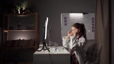 Bir çocuk blogcu, aboneleri için fen dersleri kaydederken bir laboratuarda oturuyor ve basit kimyasal deneyler yapıyor. Boşluğu kopyala