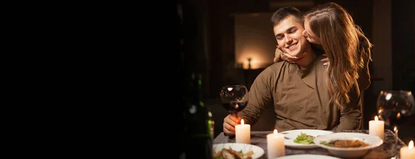Romantic dinner date with candles. Happy young couple in love having bonding, hugging, drinking wine, enjoying tender moment together. Valentines day at cozy home. Copy space