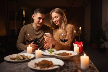 Romantik randevularda veya sevgililer gününü evde kutlarken akıllı telefondan fotoğraf çeken mutlu genç çift. Boşluğu kopyala