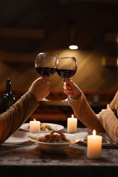 Close up of couple clinking and drinking with glasses of red wine at restaurant. Celebrating Valentines Day concept
