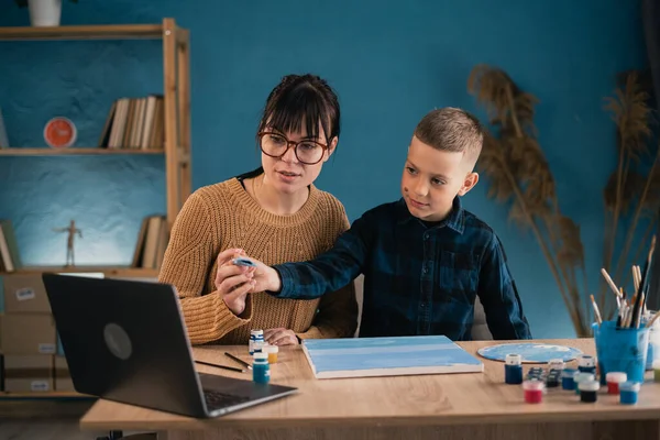 Cute boy taking online art class with mother helping him. Child and parent drawing together to video tutorial. Copy space
