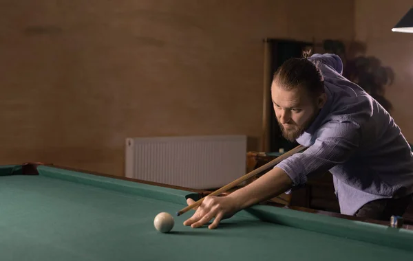 A man playing billiards at a pool table in dim light. Nightlife and leisure concept. Copy space