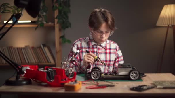 一个非常专心致志的男孩在他的房间里修理一辆破了的玩具车 在家里为孩子们焊接电线和零件 同时做他最喜欢的嗜好 复制空间 — 图库视频影像
