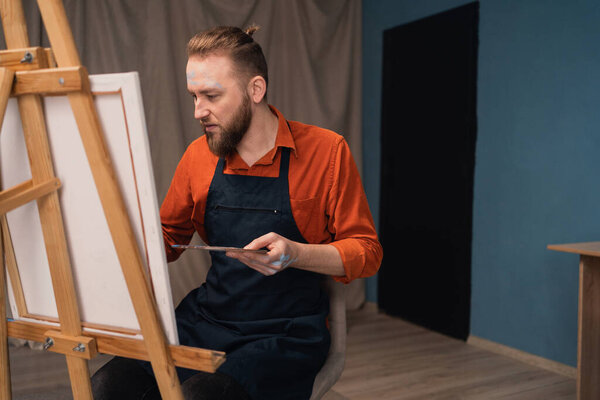 Красивый мужчина рисует что-то современное на белом холсте в студии современного искусства. Копирование пространства