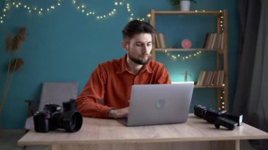 Hafıza kartındaki erkek fotoğrafçı fotoğrafı laptopta çalışan yakışıklı bir adamın ev ofisinde kamerayla çalıştığını gösteriyor. Boşluğu kopyala