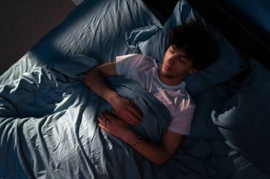 Geceleri yatak odasında bir yatakta uyuyan Arap genç adamın en iyi görüntüsü. Pencereden süzülen mavi gece ışığı. Boşluğu kopyala