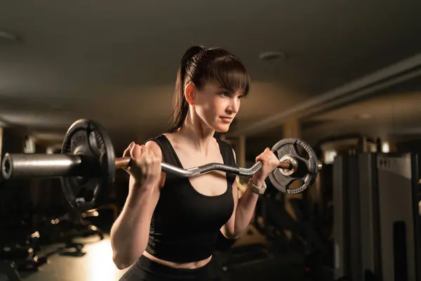 Beautiful woman does exercises for biceps uses barbell with a curved bar. Women in the gym. Copy space