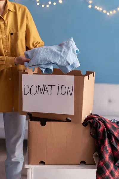 Donation Concept. Woman putting clothes in Donate Box at home. Close-up