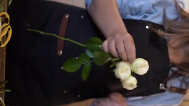Çiçekçide çiçek buketi yapan kadın dekorasyon ve düzenlemeler yapıyor. Dikey video