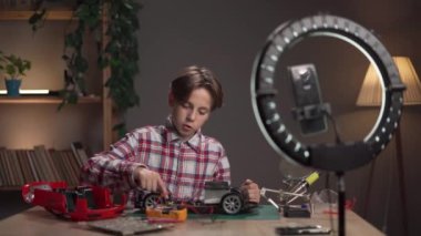 Genç blogcu akşamları ev ofisinde bir araba oyuncağını lehimliyor. Boşluğu kopyala