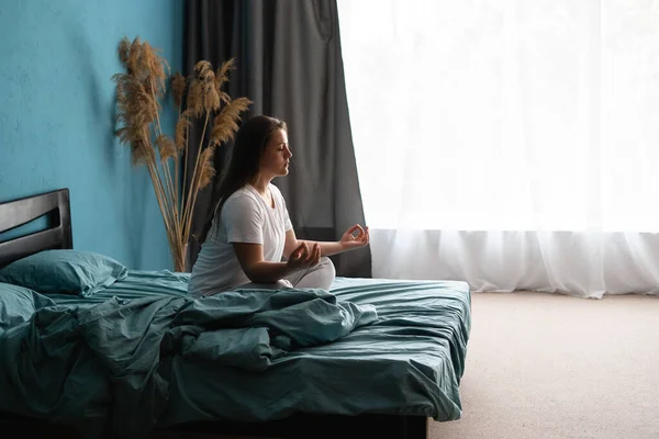 Morning meditation. Young relaxed woman practicing yoga zen on bed after waking up. Copy space