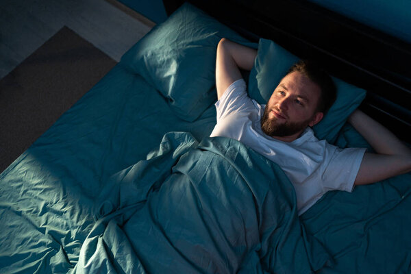 Стресс мужчина чувствует себя от бессонницы, пытаясь спать ночью в своей постели. Копирование пространства