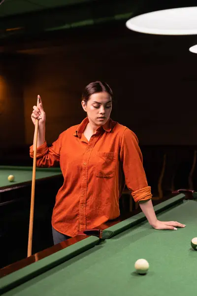 Beautiful woman standing near a pool table with a cue in her hands preparing to start the billiards game. Copy space