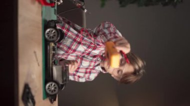 Beyaz çocuk robot araba lehimlemekle meşgul. Çocuk elektronik aletleri öğreniyor ve bir oyuncağı tamir ediyor ve ev sınıfında uzaktan kumanda kuruyor. Dikey video
