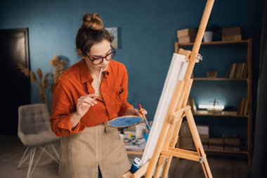 Stüdyosunda tuvale resim yapan genç, profesyonel bir kadın sanatçı. Kadın ressam atölyede resim yapıyor. Boşluğu kopyala