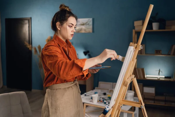 Creative latin female artist standing working on a new painting. Happy young lady painting on canvas in her art studio. Artist working in her home workshop. Copy space