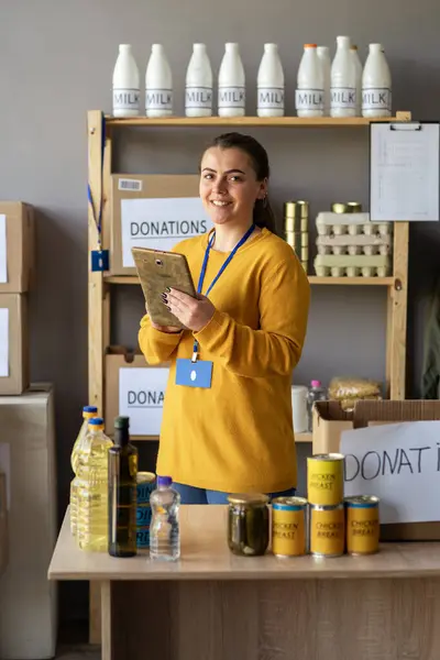 Happy smiling female volunteer with digital tablet and food in box working at distribution or refugee assistance center. charity, donation and volunteering concept. Copy space