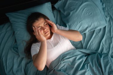 Yatakta yatan yorgun bir kadın sabahın erken saatlerinde endişeli uykusuzluk ve baş ağrısından muzdarip olarak uyanır. Kız yorgun, sağlıksız migren ve baş ağrısı konsepti hissediyor. Üst Manzara. Boşluğu kopyala