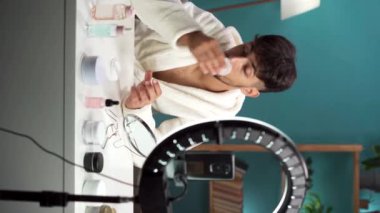 Toner uygulanıyor. Müslüman adam kameraya beyaz pamuklu bez ile yüzünü temizliyor. Sosyal medya için akıllı telefondan video bloğu kaydediliyor. Dikey video