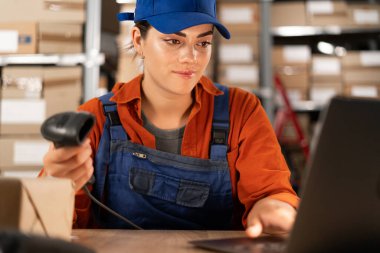 Depo çalışanı barkod tarayıcısı kullanıyor. Posta kutuları da arka planda. Küçük işletme sahibi depoda dizüstü bilgisayarda çalışıyor. Boşluğu kopyala