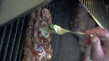 El fırçasıyla salamura sosunu barbekü etine sürdüm, yakın plan. Yemek pişirme, aşçılık ve yemek konsepti. Dikey video