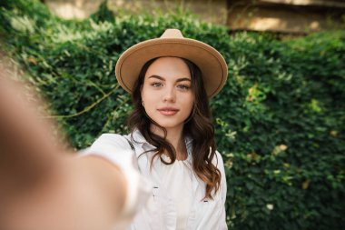 Parkta, saman şapkalı güzel, gülümseyen bir kadının portresi. Seyahat konsepti. Selfie