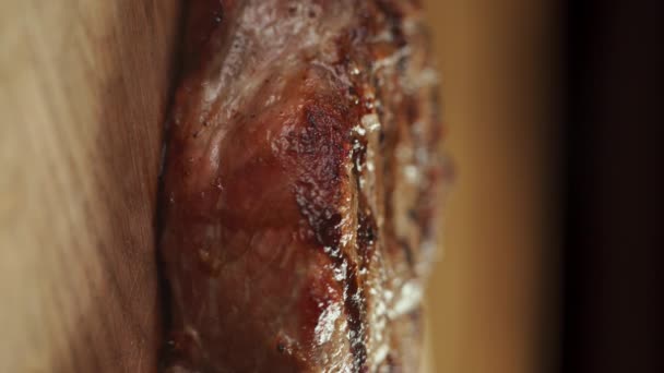 ナイフとフォークで焼き上げた牛肉バーベキュー カッティングボードにソースを入れたステーキをクローズアップします バーティカルビデオ — ストック動画