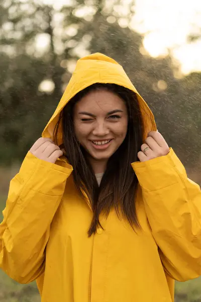 Young woman wearing yellow raincoat during the rain in the park enjoying the rain outdoors. Copy space