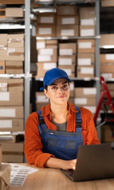 Depoda dizüstü bilgisayarla eşya envanteri yaparak çalışan bir kadın yönetici. Kameraya bakıyorum.