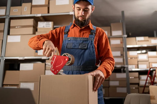 Depoda kaset kullanarak online siparişleri paketleyen yakışıklı genç adam. Boşluğu kopyala