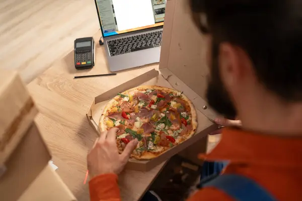 Man with pizza at laptop at warehouse. Content research and guy at desk, working at startup, eating fast food. Copy space