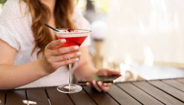 Yazın kafede çilekli smoothie içen genç bir kadın buluşmayı beklerken akıllı telefon kullanıyor. Pankart. Yakın plan.