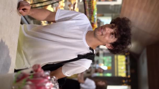 若いハンサムなアラブの男はカフェのカウンターの近くに立って アイスクリームとコーンを注文し 笑顔の男は購入に満足しています バーティカルビデオ — ストック動画