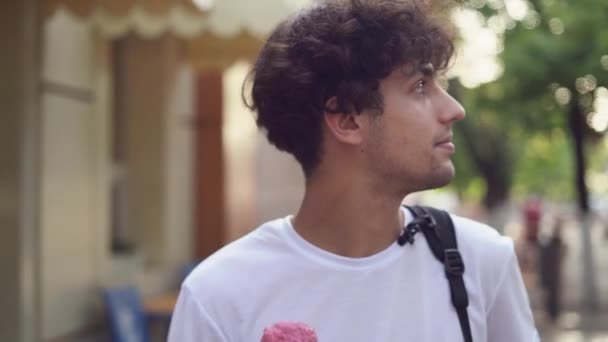夏にカーリーヘアの若い観光客アラブ人男性が街の通りを歩き アイスクリームを手にワッフルコーンを持って食べます バーティカルビデオ — ストック動画