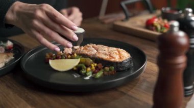 Kızarmış sebzeli ızgara somon fileto yiyen, beyaz soslu, ahşap masadaki siyah tabakta servis edilen bir kadın. Boşluğu kopyala