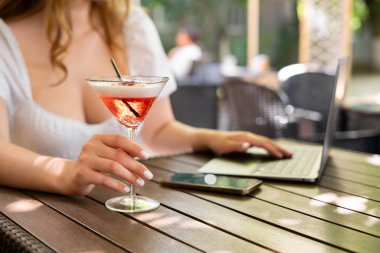 Dizüstü bilgisayarda yazı yazan ve yaz günü elinde kokteyl tutan kız. Bilgisayarla seyahat etmek. Boşluğu kopyala