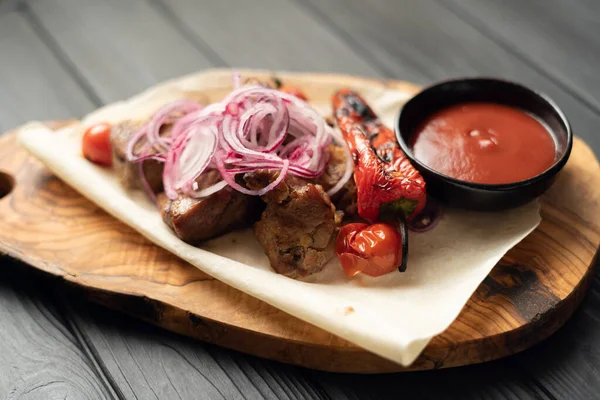 Barbecued cubed pork kebabs served with a tomato salad and onion, close up view on a wooden background. Copy space